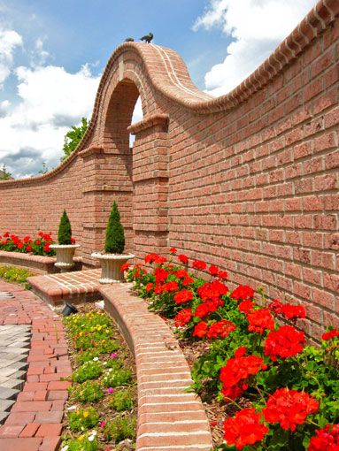 Curved garden wall with decorative brick archway and integrated floral beds